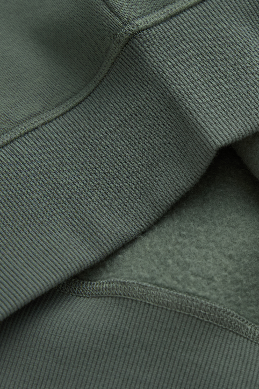Green hoodie close-up showing ribbed seam and soft fleece lining