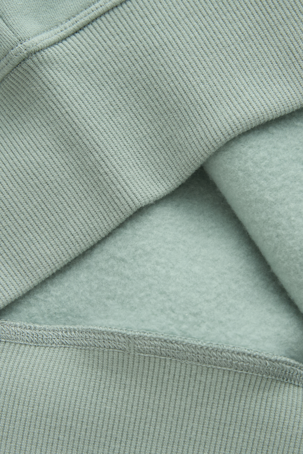 Jade hoodie fabric close-up showing soft fleece lining and ribbed seam