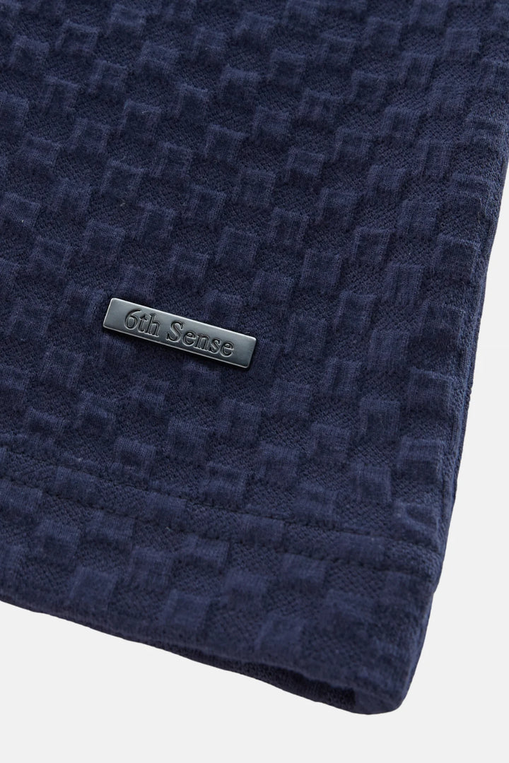 Navy jacquard polo shirt with metal brand logo patch on chest