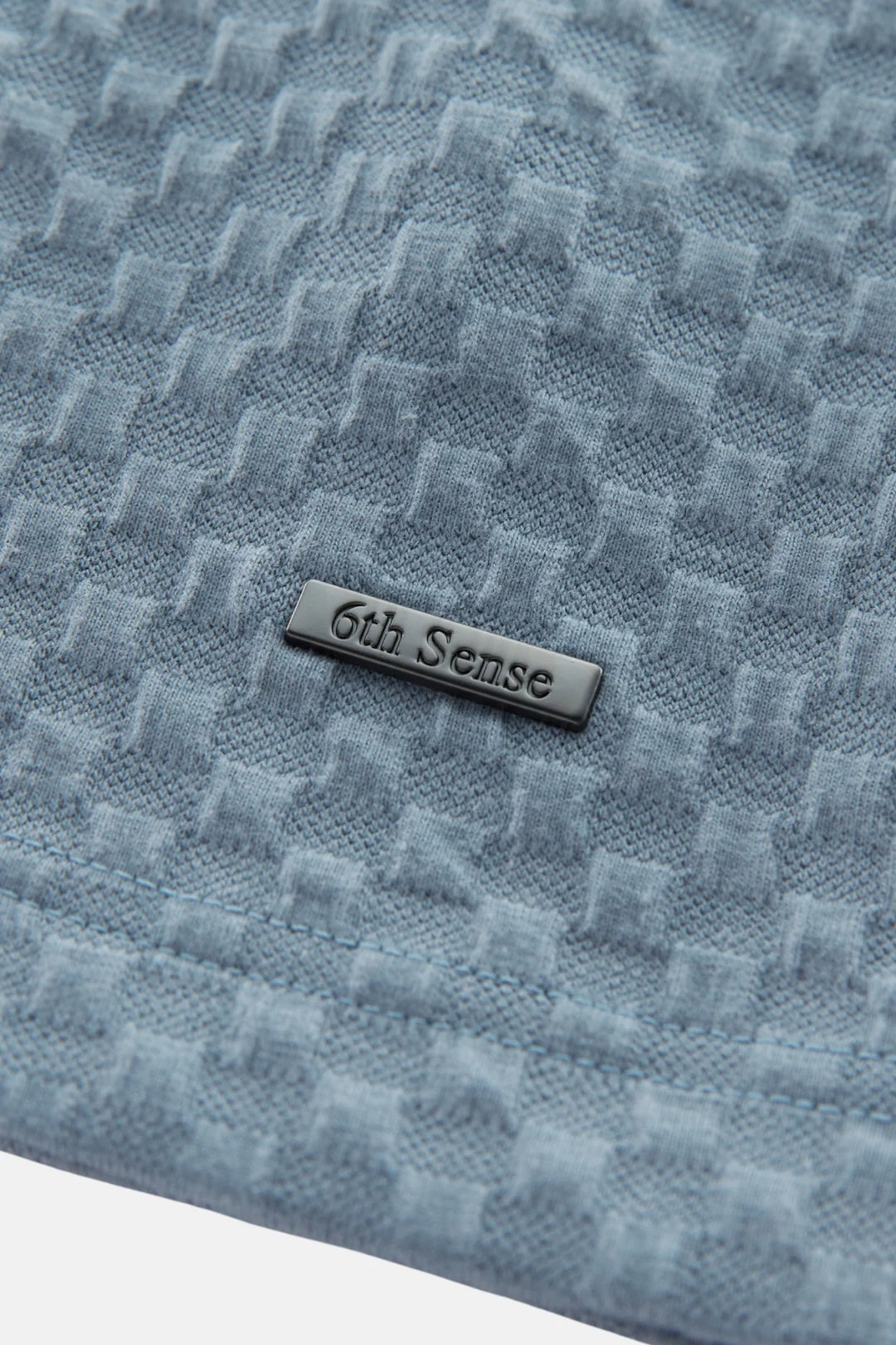 Polo shirt chest with subtle jacquard texture and 6th Sense logo tab