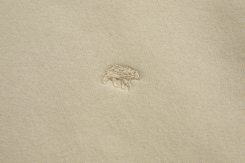 Rivet & Denim hoodie chest logo, small embroidered emblem on light feather beige