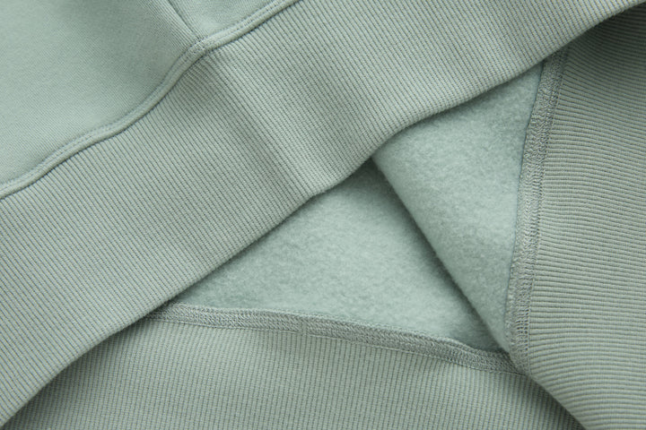 Jade denim hoodie pocket and ribbed cuff detail, showing layered construction and stitching.