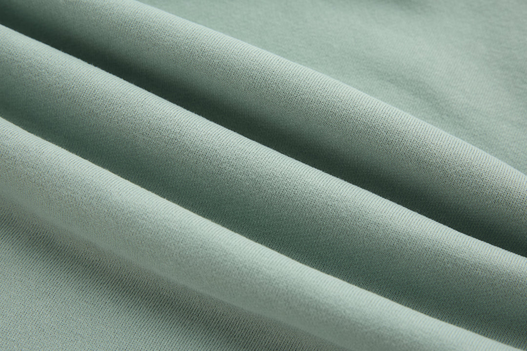 Jade denim hoodie fabric close-up, smooth textured weave in light green tone.