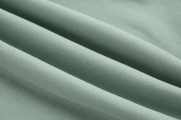 Jade denim hoodie fabric close-up, smooth textured weave in light green tone.