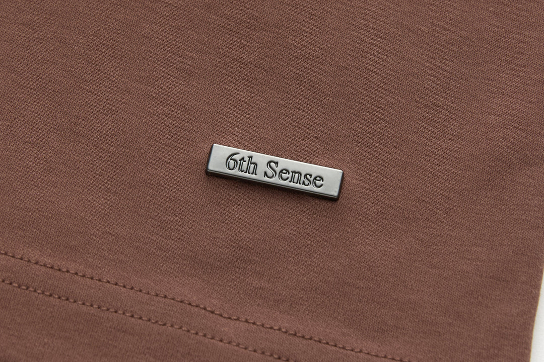 Brown t-shirt with embossed '6th Sense' metal tag at chest