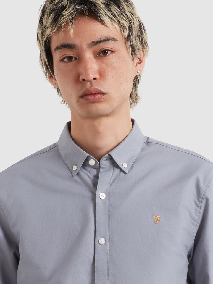 Men's light blue Oxford shirt close-up, button-down collar and embroidered chest logo.