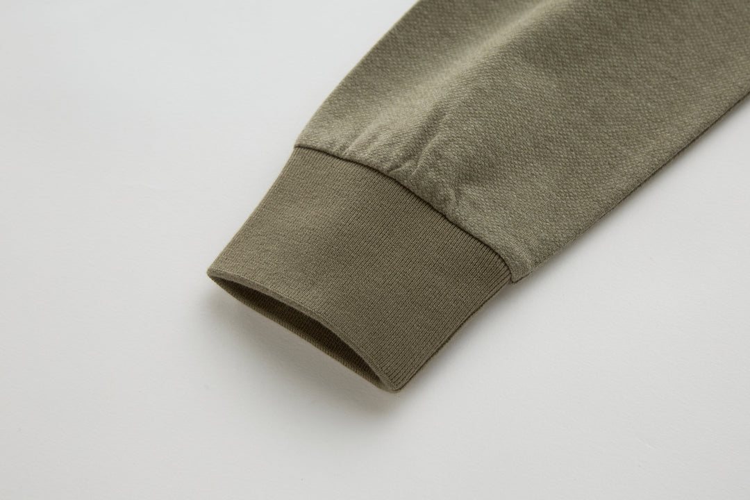 Brindle long-sleeve polo shirt cuff, olive-brown fabric with clean hem.