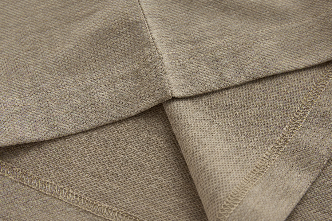 Beige long-sleeve polo shirt hem with stitched seams and knit texture.