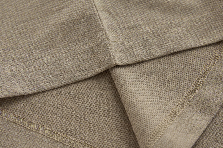 Beige long-sleeve polo shirt hem with stitched seams and knit texture.