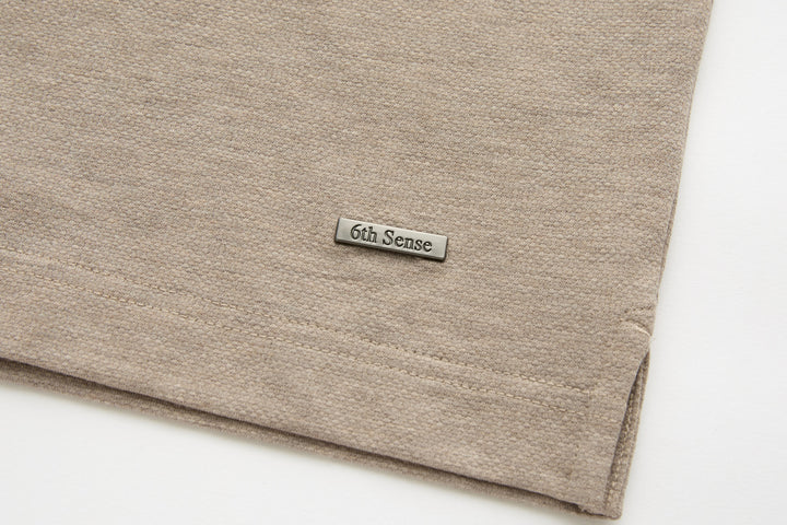 Beige polo shirt hem with small 6th Sense logo tag on front