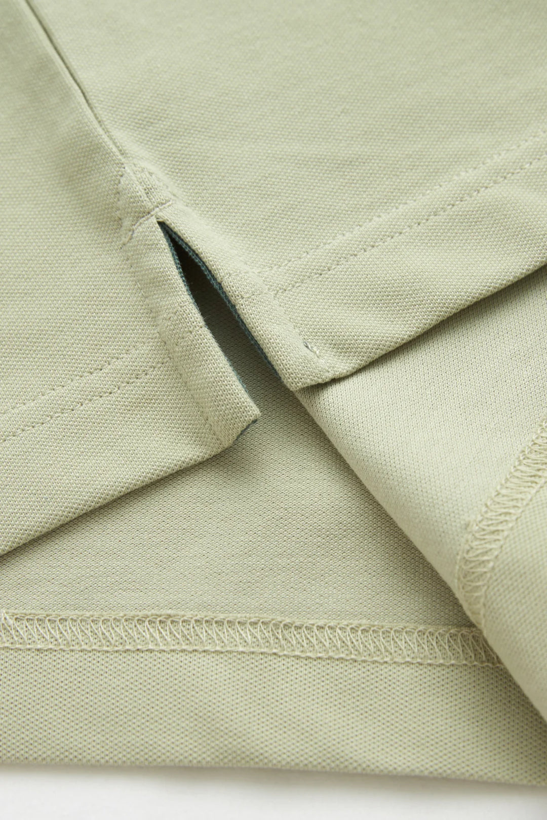 Light green polo shirt fabric close-up with folded placket and seam details